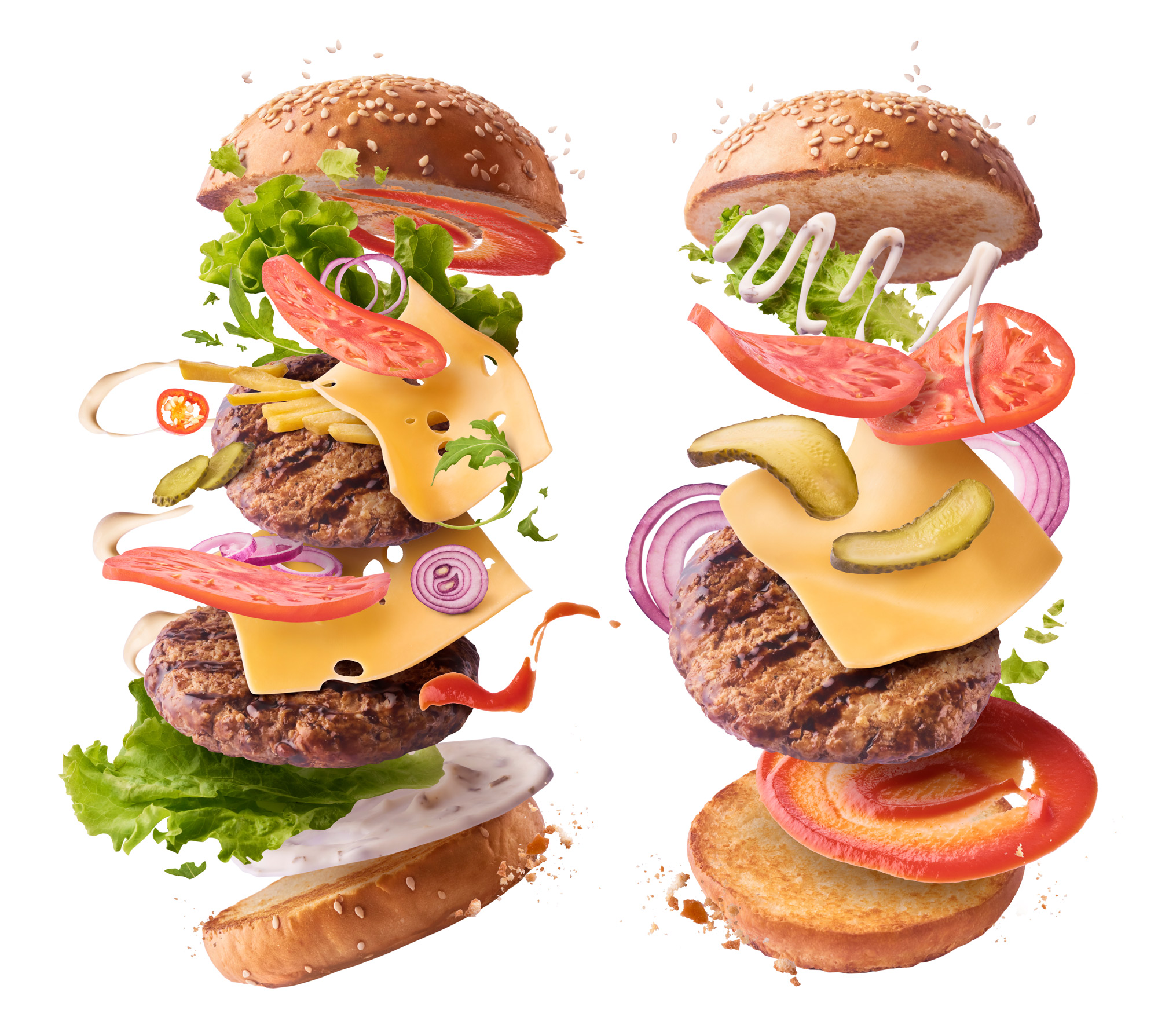 Zwei schwebende Burger mit Sesambrötchen, Salat, Tomaten, Käse, Zwiebeln, Gurken, Patties und Saucen vor weißem Hintergrund